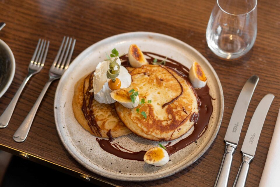 Fluffy buttermilk pancakes drizzled with rich chocolate sauce and topped with caramelised banana, served as a decadent Shrove Tuesday treat.