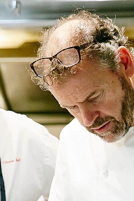 Professional chefs meticulously plating a sophisticated fine dining dessert in a bustling culinary kitchen.