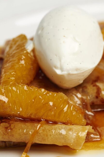 A beautifully plated serving of classic French Crêpes Suzette, accompanied by a rich Grand Marnier sauce and vanilla ice cream.