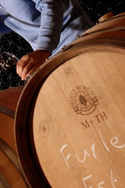 A dedicated winemaker carefully testing maturing wine directly from an oak barrel in the cellar.