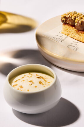 Memory of Bruschetta at Galvin La Chapelle, featuring a small white bowl of creamy foam dusted with powder, alongside a slice of pastry topped with piped chocolate and chopped nuts.