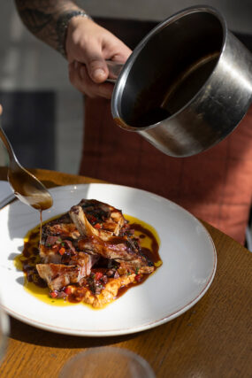 A server pouring rich jus over a plated main course of sliced lamb and puree for the New Year's Eve menu at Galvin Green Man in Essex.