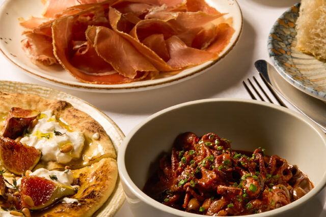 Autumn Table starters at Galvin Bistrot & Bar, showcasing a fig and cheese flatbread with pine nuts, a bowl of baby squid in tomato sauce, a plate of thinly sliced cured ham, and fresh bread with olive oil.