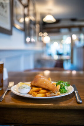 A plate of freshly prepared fish and chips served with mushy peas and tartar sauce on a wooden table inside the Galvin Green Man pub.