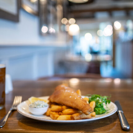 A plate of freshly prepared fish and chips served with mushy peas and tartar sauce on a wooden table inside the Galvin Green Man pub.