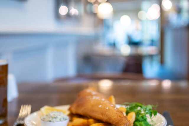 A plate of freshly prepared fish and chips served with mushy peas and tartar sauce on a wooden table inside the Galvin Green Man pub.