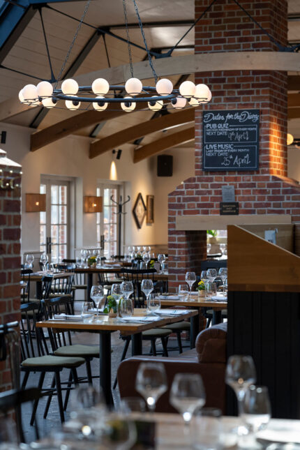 Interior of the Galvin Green Man dining room featuring set tables with wine glasses, exposed brick pillars, and a large circular chandelier.
